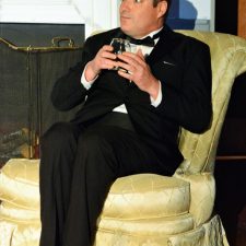 Charles sitting in yellow chair holding a drink with both hands
