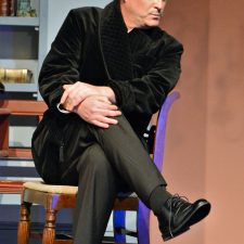 Charles Condomine sitting in chair with legs crossed