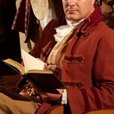 Joe-Michael Jackson in costume reading a book while acting in 1776