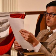 Joe-Michael Jackson wearing a suit and glasses reading a paper while acting in On Golden Pond