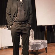 Joe-Michael Jackson in black suit, standing on stage while acting